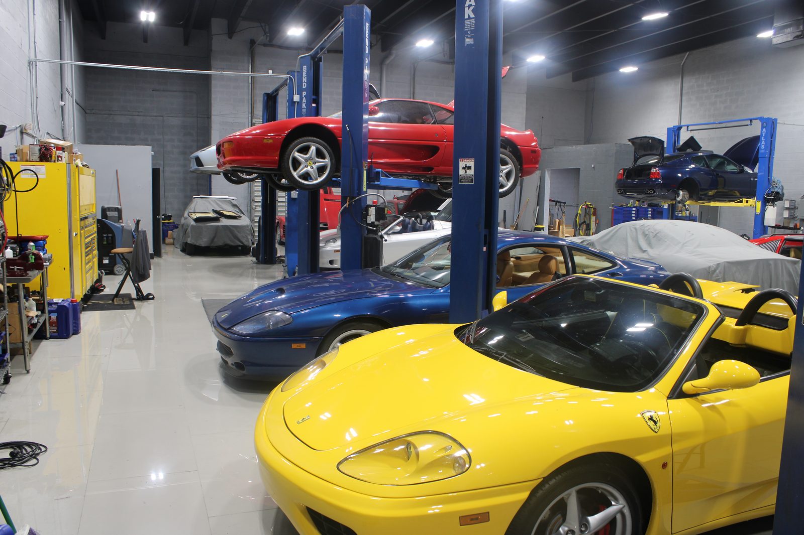 Yellow Ferrari Spider beside lifted vehicles in service